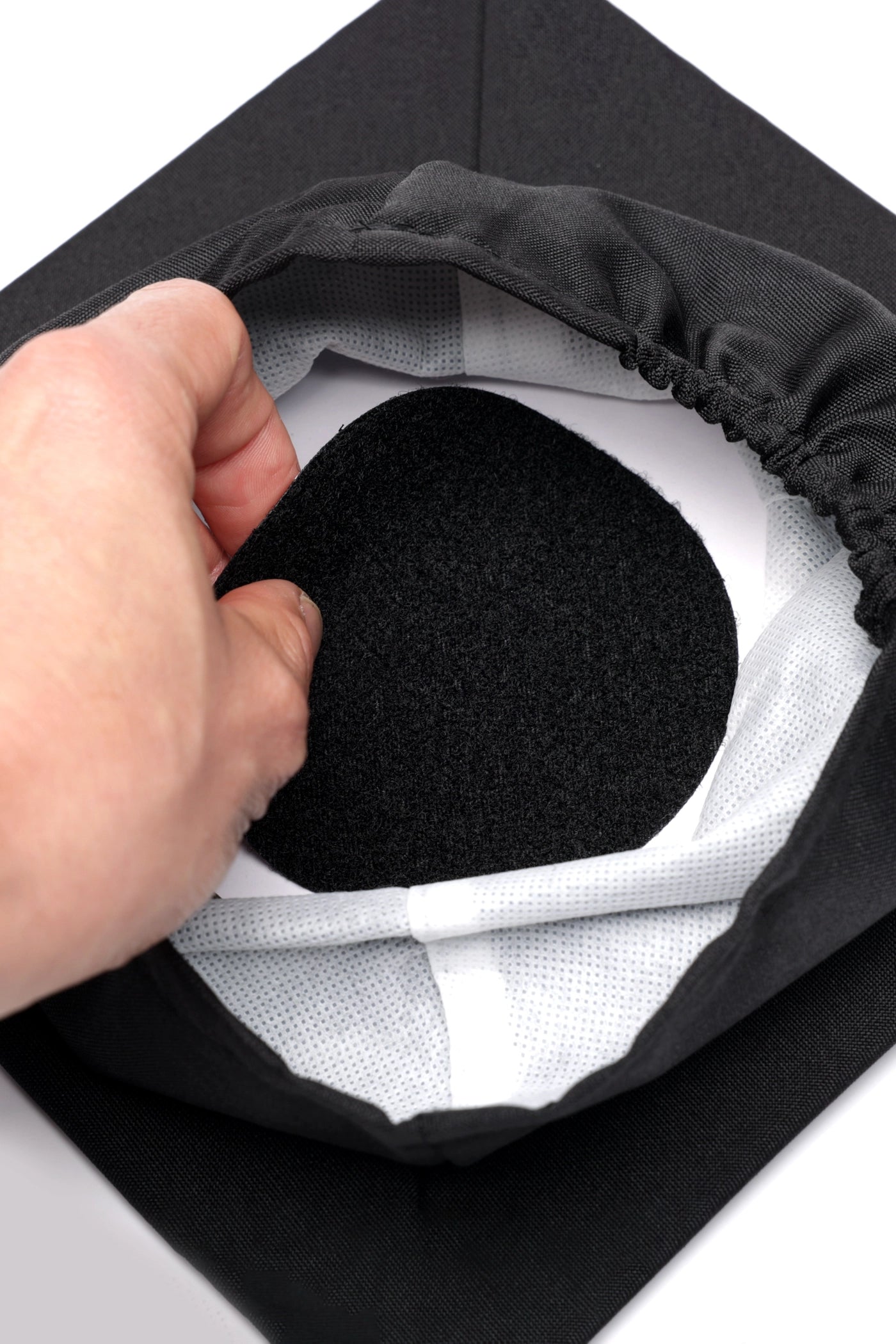 A hand puts the adhesive side of the CAPGOWN capstay headband to the top of the CAPGOWN mortarboard cap.